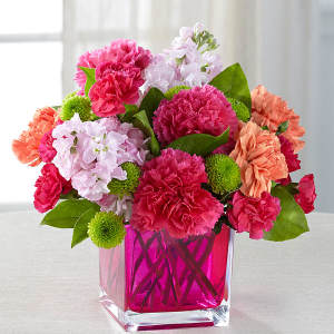Pink and peach carnations with light purple flowers in a pink glass vase