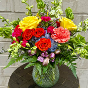 Colorful bouquet of roses, carnations, and other blooms in a textured glass vase