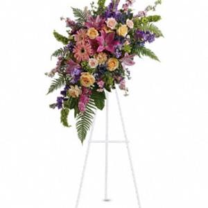 Tall standing spray of pink lilies, roses, and mixed flowers on a white easel
