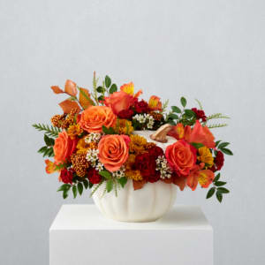 Orange and red floral arrangement in a white pumpkin vase