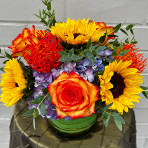 Bright mixed bouquet with sunflowers, roses, and purple hydrangea in a green vase