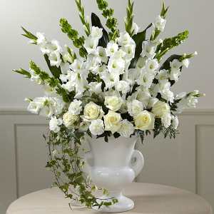 White floral arrangement in a white urn vase with trailing ivy