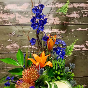 Tropical floral arrangement with orange lilies and blue flowers in a low container