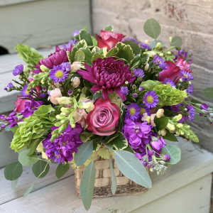 Mixed pink and purple flower arrangement in a woven basket