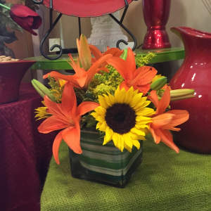 Orange lilies and a sunflower in a square glass vase
