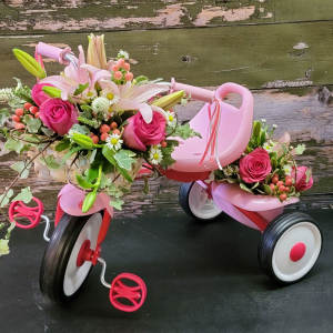 Pink floral arrangements on a small tricycle with white lilies and roses