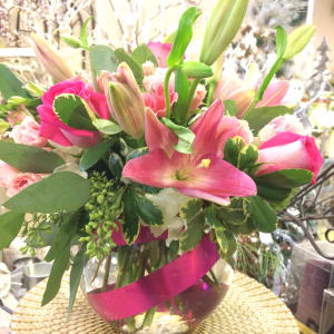 Pink lilies and roses arranged in a glass vase with a magenta ribbon