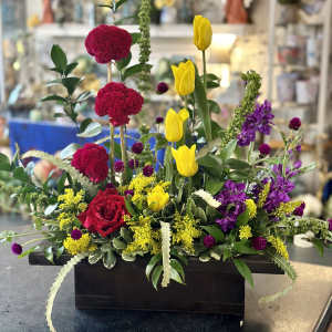 Mixed floral arrangement with red roses, yellow tulips, and purple blooms in a black container