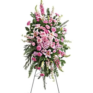 Tall standing spray of pink and white roses, lilies, and carnations on a metal easel.