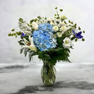 Blue hydrangea bouquet with white lilies and white flowers in a glass vase
