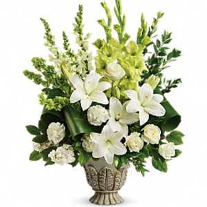 Tall arrangement of white lilies, roses, and carnations with green accents in an ornate ivory urn vase
