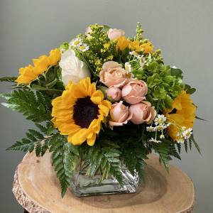 Mixed bouquet with sunflowers, blush roses, and white daisies in a glass vase