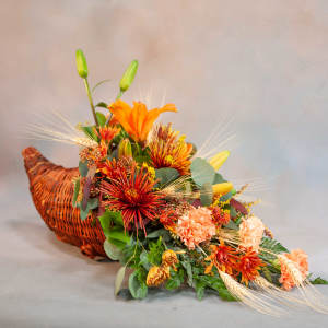 Orange floral arrangement in a woven basket with lilies and mums