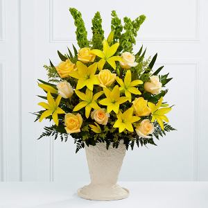 Yellow roses and lilies arranged in a cream pedestal vase