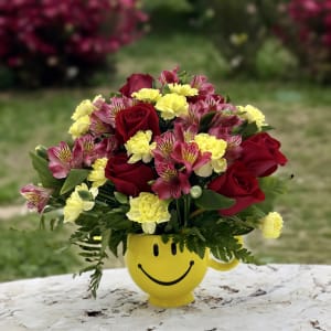 Bouquet of red roses, pink alstroemeria, and yellow carnations in a smiley-face mug