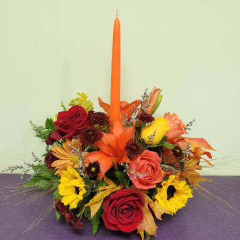 Autumn floral centerpiece with roses, sunflowers, and a tall orange taper candle