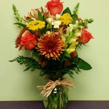 Mixed bouquet of orange roses, yellow blooms, and chrysanthemums in a glass vase