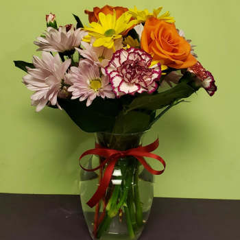 Mixed bouquet of daisies, roses, and carnations in a glass vase with a red ribbon