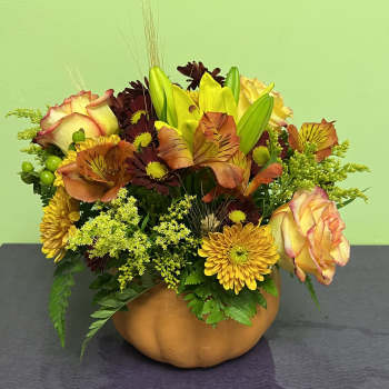Autumn floral arrangement in a pumpkin-shaped container with roses and lilies