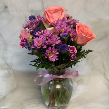 Pink roses and purple daisies in a glass vase with a ribbon