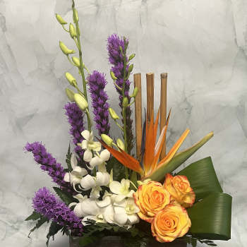 Tropical floral arrangement with orange roses, white orchids, and purple spikes in a wooden box