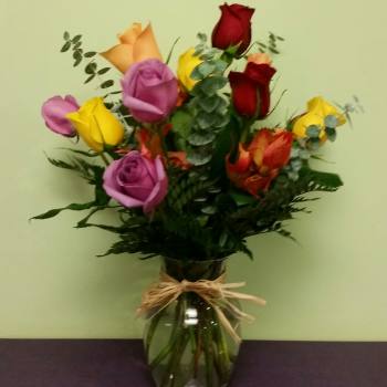 Bouquet of multicolored roses in a glass vase with a raffia bow