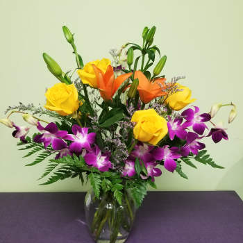 Mixed bouquet of yellow roses, orange lilies, and purple orchids in a glass vase