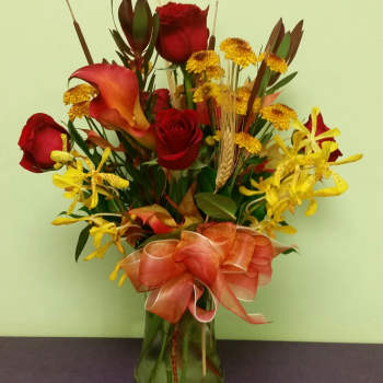 Bouquet of red roses, yellow orchids, and calla lilies in a glass vase