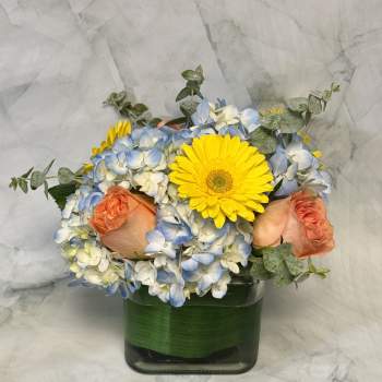 Bouquet of blue and white hydrangeas with yellow gerbera daisies and peach roses in a glass vase