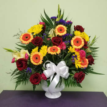 Mixed bouquet of red roses, yellow daisies, and orange gerberas in a white vase