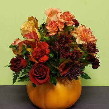 Autumn floral arrangement in a pumpkin-shaped container with roses and carnations