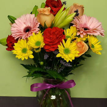 Mixed bouquet of pink, red, yellow, and peach flowers in a glass vase