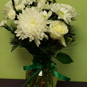 White flowers arranged in a glass vase with a green ribbon