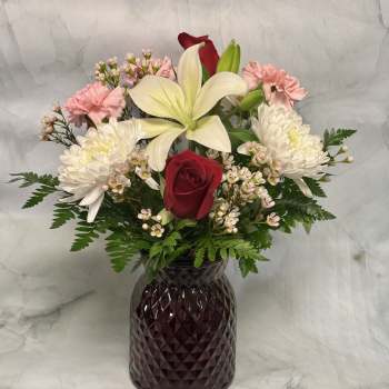 Mixed bouquet with red roses, white lilies, and pink carnations in a dark vase