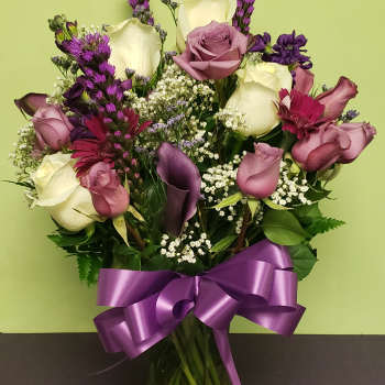 Mixed bouquet of roses, calla lilies, and purple flowers in a glass vase with a ribbon