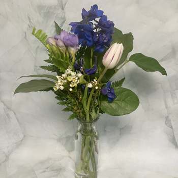 Mixed bouquet of blue, lavender, and white flowers in a clear glass vase