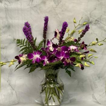 Purple orchids and tall purple spikes in a clear glass vase