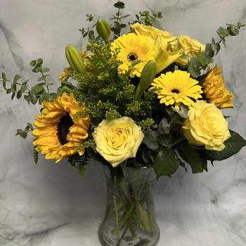 Yellow roses and sunflowers in a clear glass vase