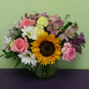Mixed bouquet with a sunflower, pink roses, and white daisies in a glass vase