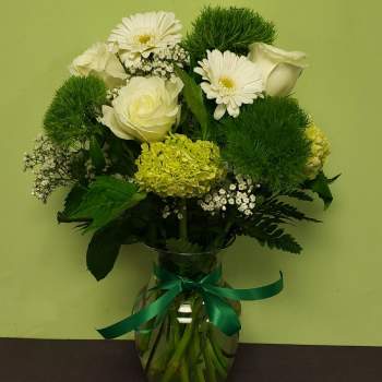 White flowers and green blooms arranged in a glass vase with a ribbon
