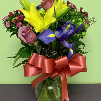Bouquet of yellow lilies, purple irises, and pink roses in a glass vase with a red ribbon
