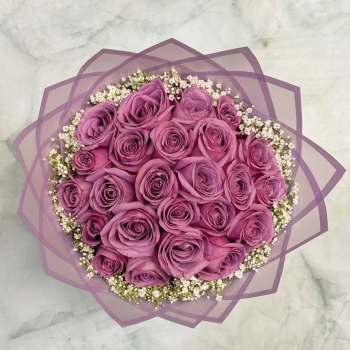 Round bouquet of purple roses with white filler flowers wrapped in lavender paper