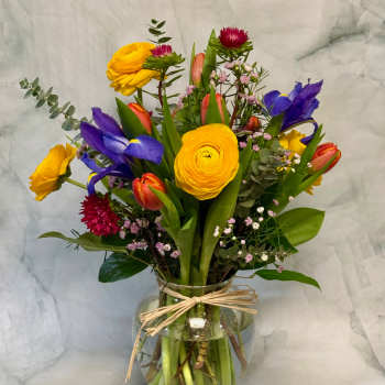 Mixed bouquet in a glass vase with yellow, purple, and coral blooms