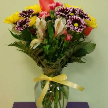 Mixed bouquet of colorful flowers in a glass vase with a yellow ribbon