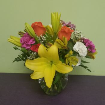 Mixed bouquet with yellow lilies, orange roses, and pink carnations in a glass vase