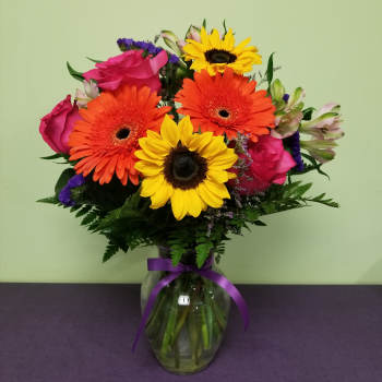 Bouquet of sunflowers, gerbera daisies, and pink roses in a glass vase