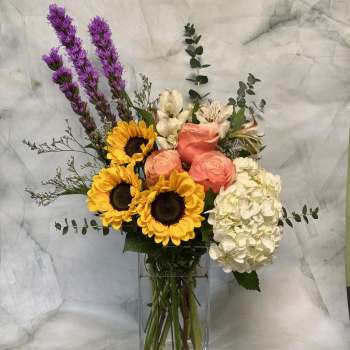 Bouquet of sunflowers, roses, and hydrangea in a glass vase