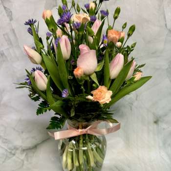 Pink tulips and peach carnations in a glass vase with a ribbon