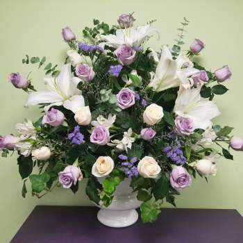 Lavender roses and white lilies arranged in a white vase