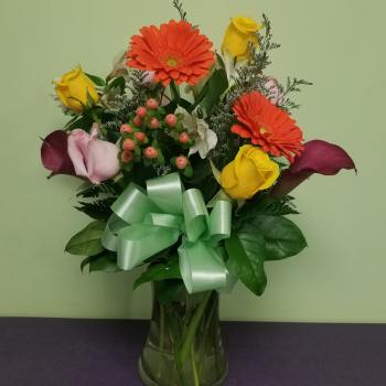 Bouquet of yellow roses, orange gerberas, and purple calla lilies in a glass vase